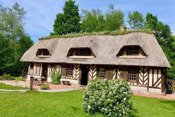 Ein traditionelles reetgedecktes Cottage mit symmetrischer Fassade, einer kleinen Veranda und einem gepflegten Garten.