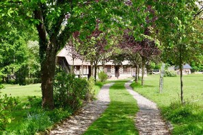Ein Weg, der zu einem traditionellen Gebäude mit Strohdach führt, umgeben von üppigem Grün und Bäumen.