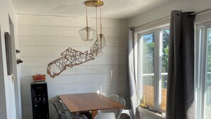 A dining area with a wooden table, white chairs, pendant lights, a water dispenser, and a window with curtains.