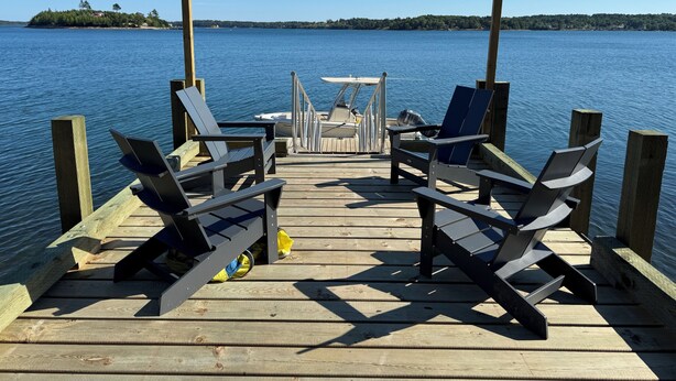 A wooden dock with two Adirondack chairs and a small table, overlooking a calm lake with a distant shoreline.