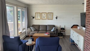 A living room with a sofa, two armchairs, a coffee table, a TV, and framed pictures on the wall.