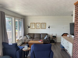 Una sala de estar con un sofá, dos sillones, una mesa de centro, un televisor y cuadros enmarcados en la pared.