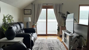 Un saló modern amb un sofà de cuir negre, un moble de televisió blanc i una finestra gran amb vista a una massa d'aigua.