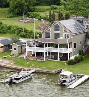 A two-story house with a large balcony, a dock with boats, and a grassy yard.