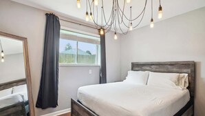 A bedroom with a bed, a mirror, a window with curtains, and a chandelier. - Fairlane #2 | Uncaged (Lansing)