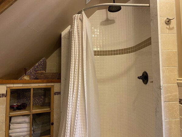 Une douche avec un rideau blanc, des murs carrelés et une étagère en bois sur laquelle se trouvent un panier et une voiture jouet.