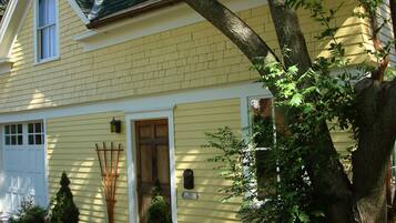 Une maison jaune avec une porte d’entrée, une boîte aux lettres et un petit arbre dans le jardin.