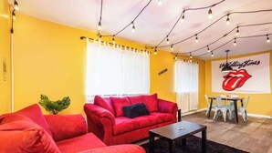 A room with a red sofa, a small table, a plant, and a Rolling Stones poster on the wall.