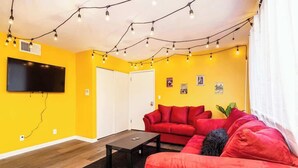 A living room with a yellow wall, a red sofa, a black coffee table, and string lights.