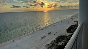 A beach with a pier in the distance, a clear sky, and the sun setting over the ocean.