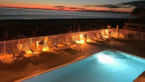 A pool area with lounge chairs and a view of the ocean at sunset.