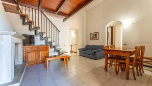 A spacious living area with a staircase, a dining table with chairs, a sofa, and a fireplace. - 3 bedroom lovely apartment in Orbetello (Orbetello)