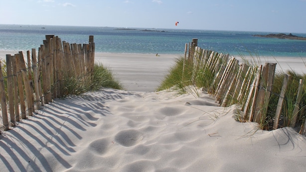 Una spiaggia sabbiosa con una recinzione in legno e una vista libera sull'oceano.