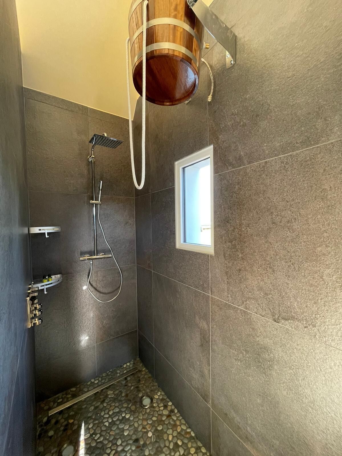 A modern shower area with a rain showerhead, a small window, and a pebble-patterned floor.