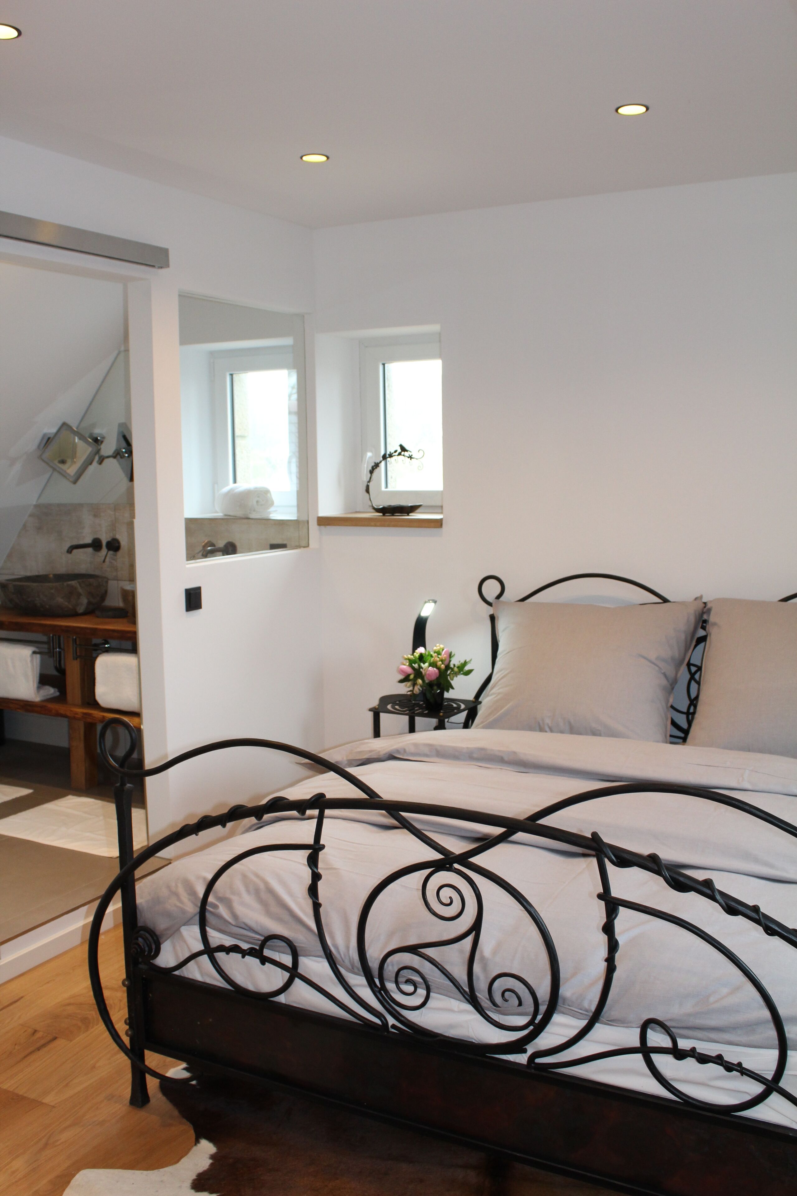 A bedroom with a bed, a bedside table with a lamp, a mirror, and a view of a bathroom.