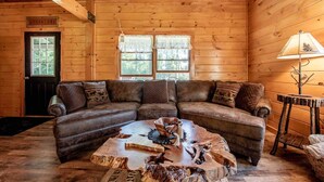 A cozy cabin interior with a wooden floor, a leather sectional sofa, a rustic coffee table, and a lamp. - Off-Grid Adventure Cabin | Peakaboo Mountain Views (Canaan)