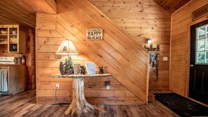 A cabin interior with a wooden staircase, a table with a lamp and framed pictures, and a sign that says "The Cabin is My Happy Place". - Off-Grid Adventure Cabin | Peakaboo Mountain Views (Canaan)
