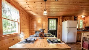 A wooden cabin with a dining table set for four, a refrigerator, and a window overlooking greenery. - Off-Grid Adventure Cabin | Peakaboo Mountain Views (Canaan)
