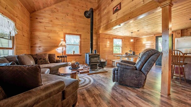 A cozy log cabin interior with a fireplace, wooden walls, a sofa, and a dining table. - Off-Grid Adventure Cabin | Peakaboo Mountain Views (Canaan)
