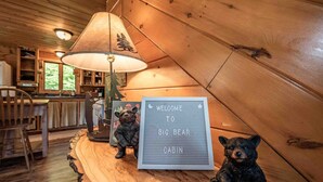 A cabin interior with a wooden table, a lamp, two bear figurines, and a welcome sign. - Off-Grid Adventure Cabin | Peakaboo Mountain Views (Canaan)