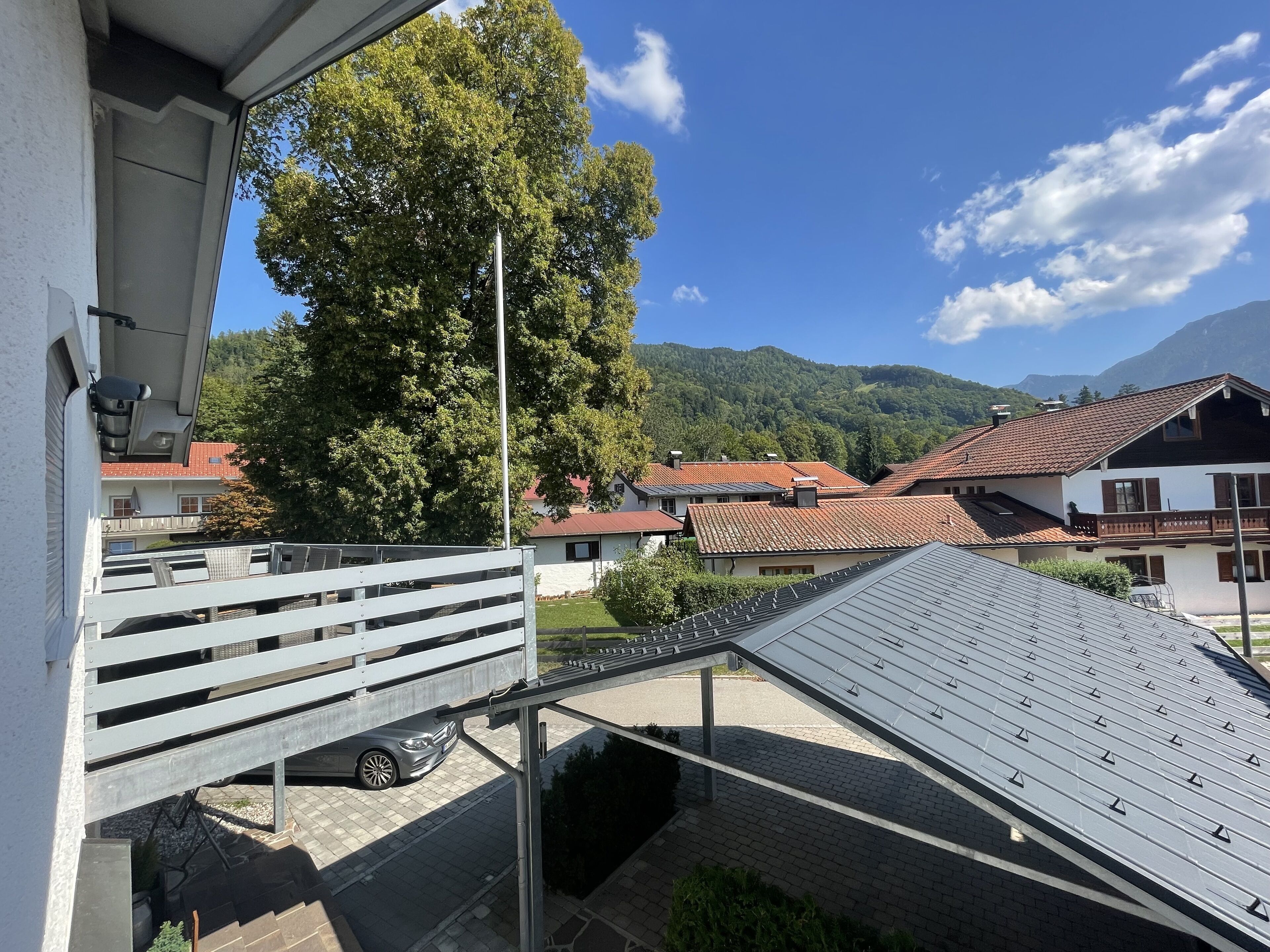 Quartiere residenziale con case, un albero secolare e una montagna sullo sfondo.