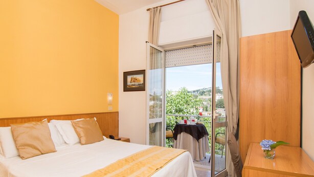 A hotel room with a bed, a desk, a TV, and a balcony with a table and chairs. - hotel villa fernanda  (Massa Lubrense)