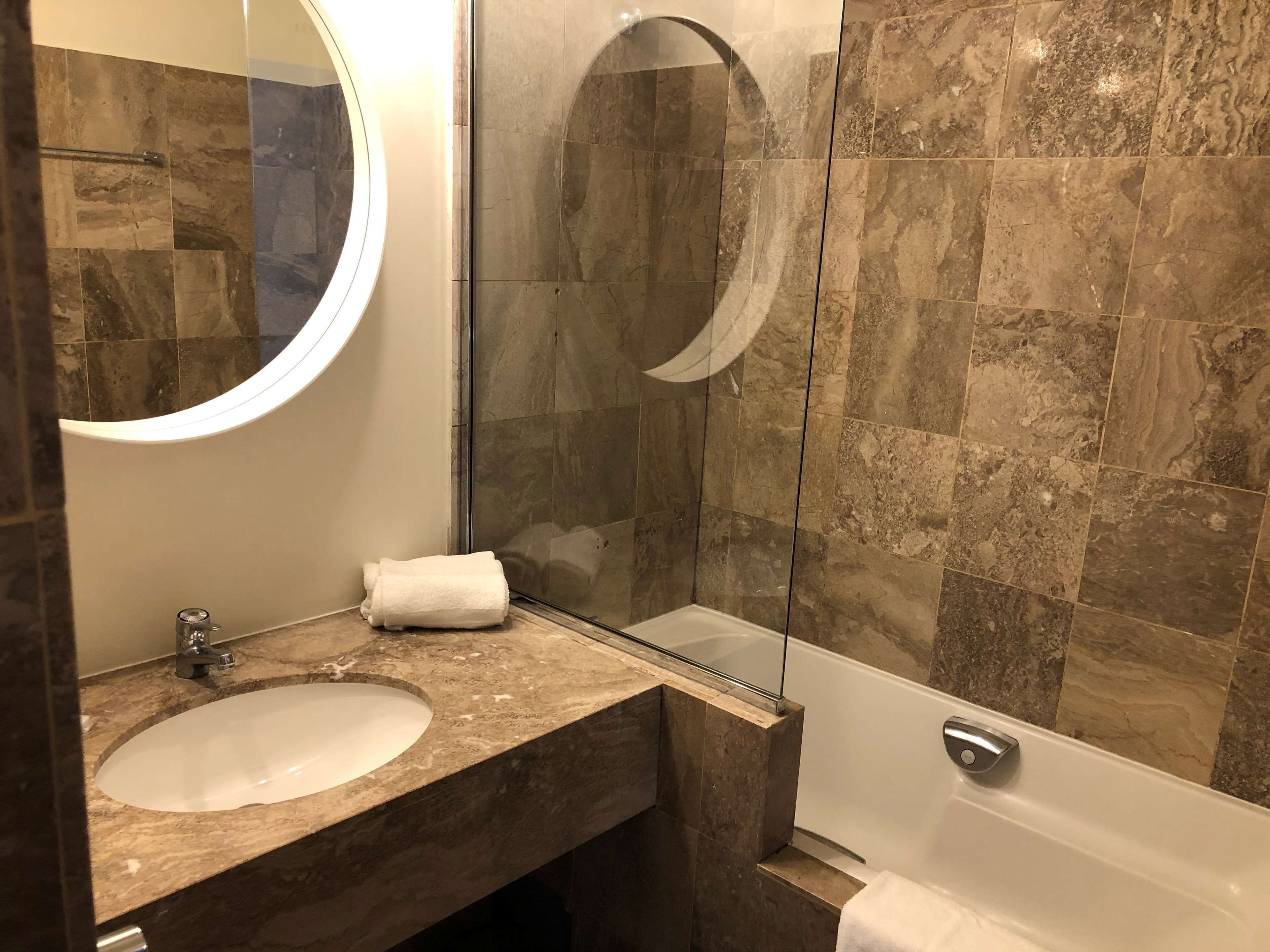 Un baño con lavamanos de mármol, espejo y ducha con mampara de vidrio.