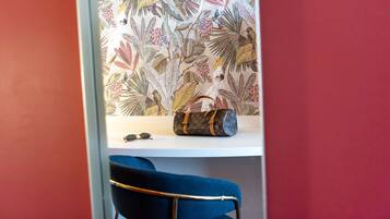 Una habitación con papel tapiz estampado, una silla azul, una mesita con un bolso de mano y gafas de sol.