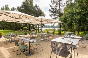 An outdoor patio area with tables and chairs, large umbrellas, and a view of a lake. - Best Western Hotel du Lac Dunkerque (Armbouts-Cappel)