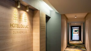 A hotel corridor with wooden walls, a carpeted floor, and a sign indicating 'HOTEL DU LAC DUNKERQUE' and 'Access to chambers'. - Best Western Hotel du Lac Dunkerque (Armbouts-Cappel)