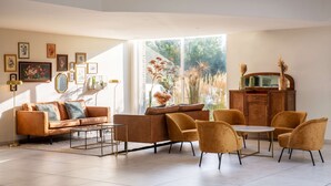 A modern living room with a sofa, chairs, a coffee table, and a cabinet. There are framed pictures on the wall and a large window with a view of greenery. - Best Western Hotel du Lac Dunkerque (Armbouts-Cappel)
