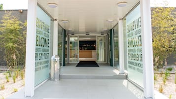 Vestíbulo moderno de edificio con mostrador de recepción, puertas de cristal y un bote de basura metálico.