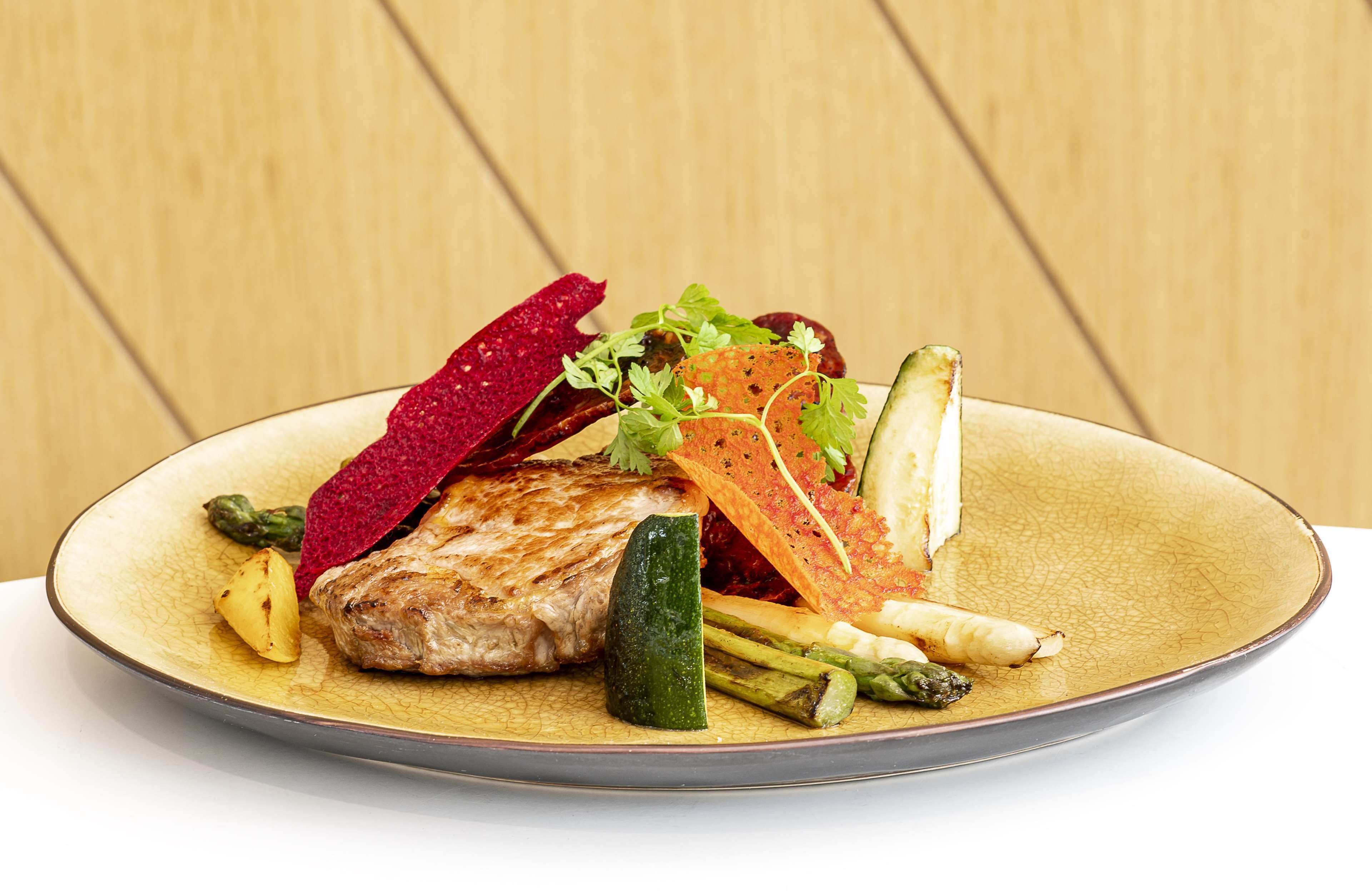 Ein Teller mit gegrilltem Fleisch, Gemüse und einer dekorativen Scheibe Rote Bete.