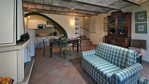 Ein gemütliches Wohnzimmer mit einem grünen Karosobensofa, eine Essecke mit einem Holztisch und Stühlen, eine Küche mit einer Mikrowelle und Schränken sowie eine Treppe, die nach oben führt.