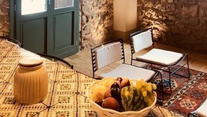 A rustic room with a stone wall, wooden ceiling beams, a patterned table, and a bowl of fruit. - Graffeo Countryside Sea View Homes in Menfi in Sicily - Casa delle Rose -  (Menfi)