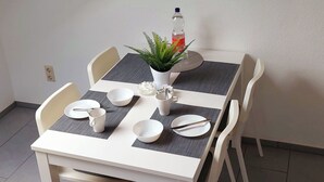 A dining area with a white table, four chairs, a potted plant, and a wall-mounted artwork. - Ferienwohnung.-monteur/geschäftsleute (Wallerfangen)