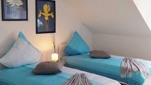 A bedroom with two beds, each with a blue bedspread and pillows, a nightstand with a lamp, and two framed floral paintings on the wall. - Ferienwohnung.-monteur/geschäftsleute (Wallerfangen)