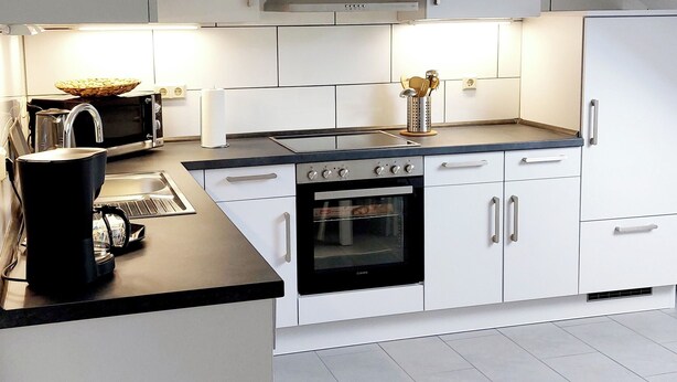 A modern kitchen with white cabinetry, a built-in oven, and a microwave. - Ferienwohnung.-monteur/geschäftsleute (Wallerfangen)