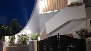 Ein modernes Haus mit einer gebogenen Fassade, einem verschlossenen Eingang und einem kleinen Balkon mit gestreiftem Markisenvorzelt.