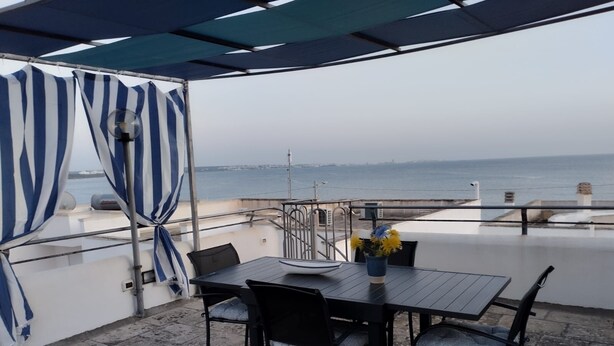 Ein überdachter Außenbereich mit Tisch und Stühlen, mit Blick auf ein Gewässer.