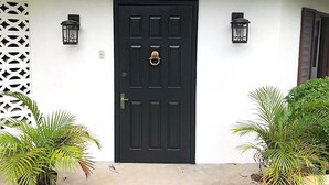 A black door with a sign above it reading "Reef Winds." There are two wall-mounted lanterns on either side of the door.