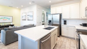 A modern kitchen with white cabinets, stainless steel appliances, and a grey sofa in the living area.
