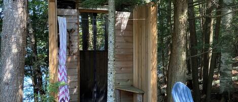 A wooden cabin with a bench and a chair outside, surrounded by trees.