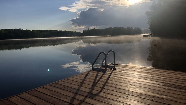 Een houten steiger die uitkomt op een rustig meer, met een zonsopgang op de achtergrond.