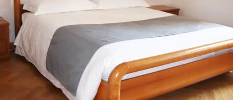 A wooden bed with a grey and white duvet in a room with wooden flooring and a nightstand.