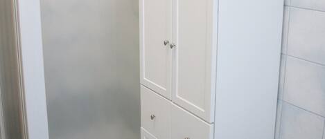 A bathroom with a shower enclosure, a toilet, and a cabinet.