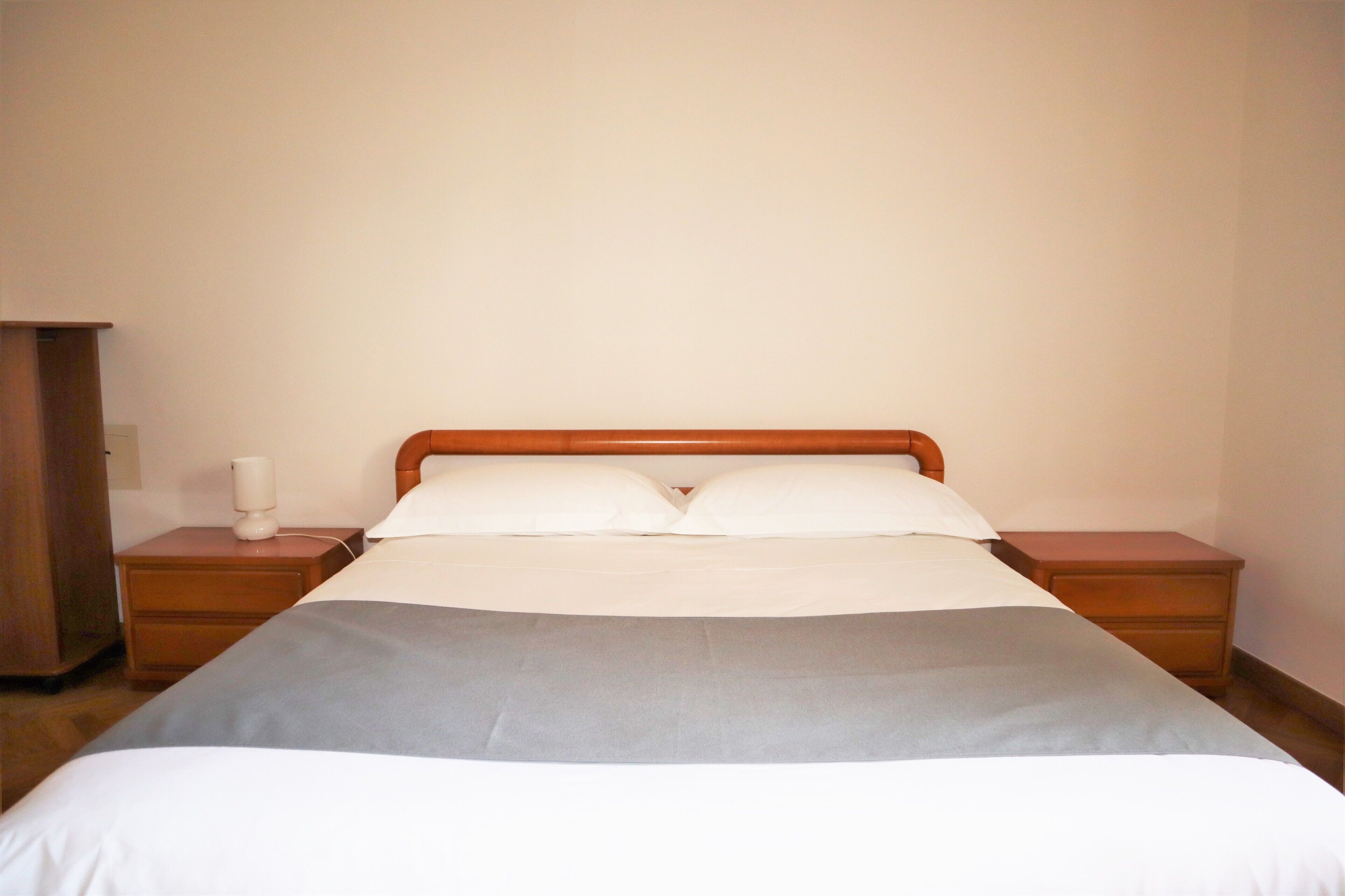 A neatly made bed with a wooden headboard, two bedside tables, and a nightstand.