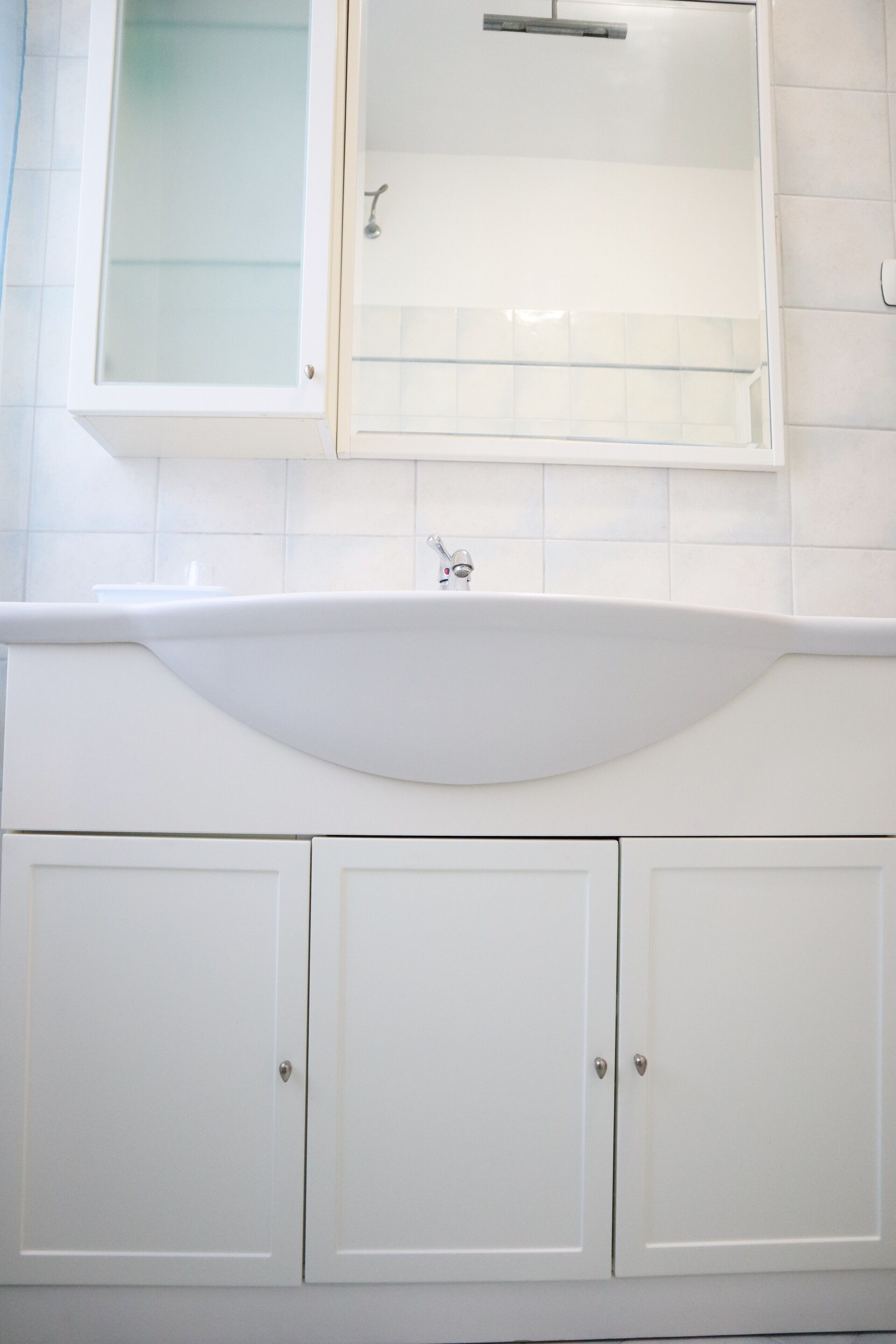 Une salle de bain avec un lavabo blanc, un meuble à pharmacie fermé par une porte en verre et des armoires blanches.