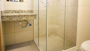 Un baño con ducha de vidrio, un lavamanos con encimera de mármol y un inodoro.