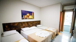 Habitación de hotel con tres camas, un cuadro de un paisaje urbano y vistas al exterior.
